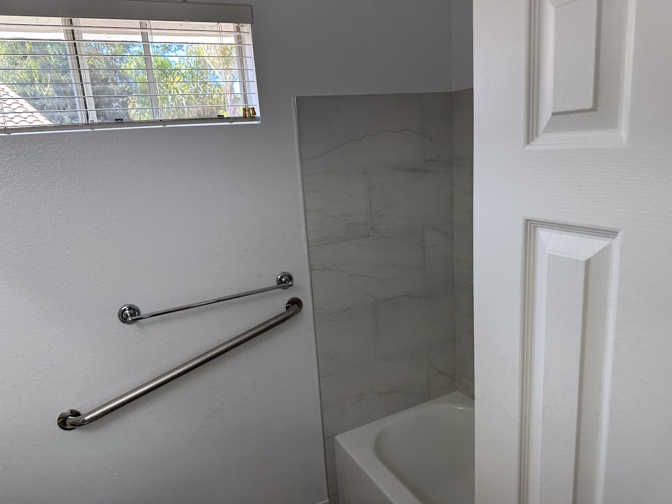 Two stainless steel wall-mounted grab bars beside a bathtub and tiled shower surround