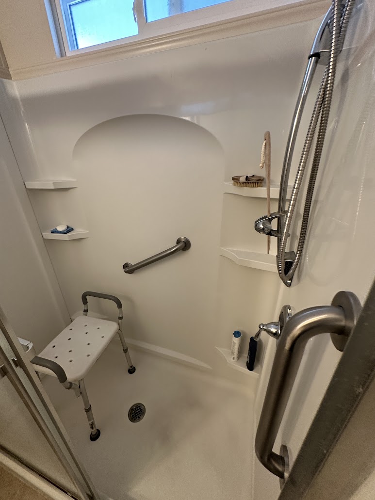 Wall-mounted grab bars in a white shower with a shower seat and handheld shower head