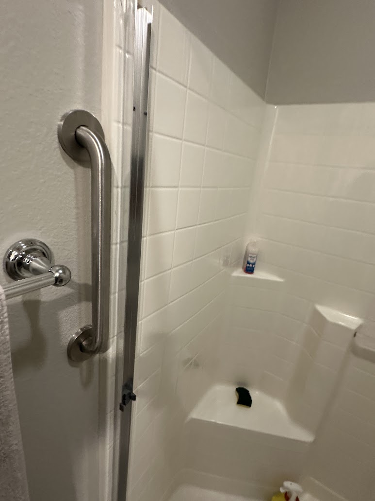 Vertical stainless steel grab bar mounted next to the entry of a white shower