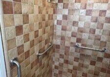 Three stainless steel grab bars installed in an Oceanside tiled shower, one vertical at the entry and two horizontal on the walls
